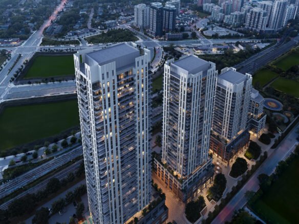 Aerial view of a modern residential high-rise complex during twilight, showcasing illuminated buildings and adjacent green spaces, with new condos in the background.