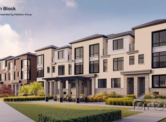 A modern Brooklin townhouse complex with three-story buildings featuring large windows, a mix of brick and light-colored exteriors. The foreground shows a landscaped area with grass, bushes, a bike rack with two bicycles, and a couple of benches. The sky is clear over the Towns.