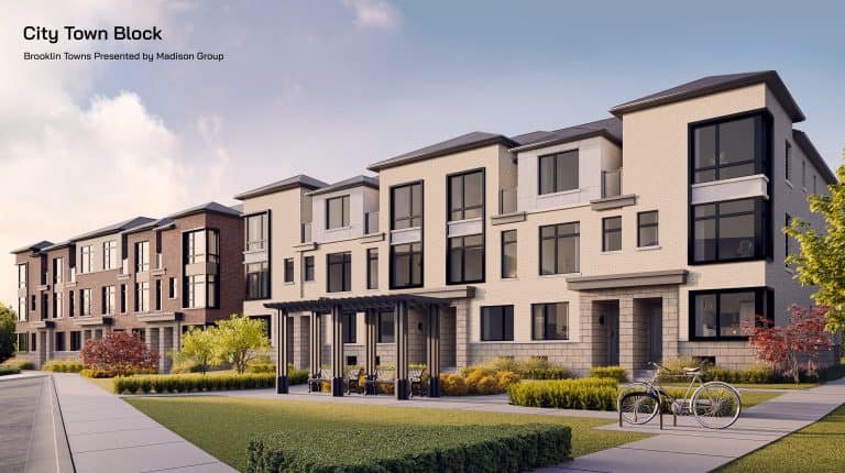 A modern Brooklin townhouse complex with three-story buildings featuring large windows, a mix of brick and light-colored exteriors. The foreground shows a landscaped area with grass, bushes, a bike rack with two bicycles, and a couple of benches. The sky is clear over the Towns.
