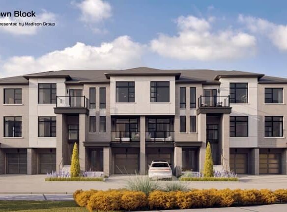 Brooklin Towns, a modern townhouse complex with three stories and multiple units, is showcased under a clear blue sky. The buildings feature large windows, balconies, and neutral-toned exteriors. A white car is parked in front of the central unit, and there is well-maintained landscaping.