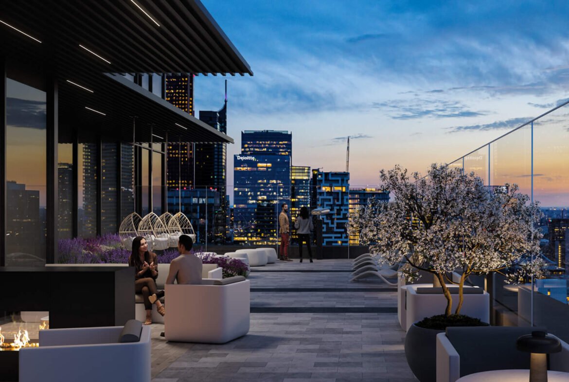 A modern rooftop patio at dusk, featuring cozy seating areas with a fire pit and potted plants, including a blossoming tree. City skyscrapers are visible in the background against a colorful sunset sky. A few people are seated, enjoying the ambiance of New Homes in GTA as they view Pre Construction Homes nearby.