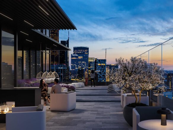 A modern rooftop patio at dusk, featuring cozy seating areas with a fire pit and potted plants, including a blossoming tree. City skyscrapers are visible in the background against a colorful sunset sky. A few people are seated, enjoying the ambiance of New Homes in GTA as they view Pre Construction Homes nearby.