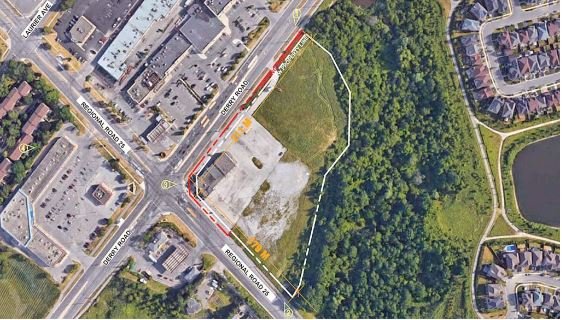 An aerial view of a commercial area with a large parking lot and various buildings. Adjacent streets include Prescott Road, Cordoba Road, and Decatur Road. To the right is a dense wooded area, while residential housing and new condos in GTA are visible nearby.