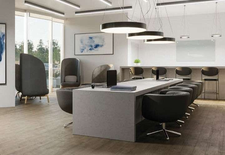 Modern office space with a large, rectangular table surrounded by swivel chairs. Hanging circular lights illuminate the area. To the left, two pod-like chairs are positioned near full-length windows, and a bar-style counter with stools is at the back—a perfect setup for discussions about new homes in GTA.