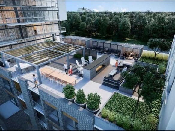 A rooftop terrace features lounge areas with outdoor furniture, a bar with stools, and a pergola providing shade. In the background, lush greenery and a body of water are visible. People enjoy the space, which is surrounded by modern buildings showcasing new condos in GTA.