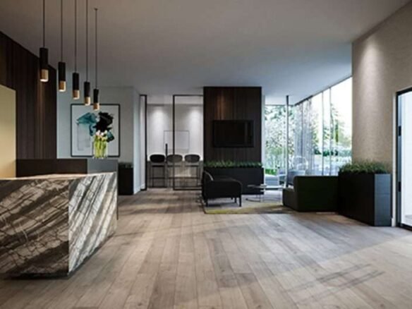 Modern minimalist interior of a lobby area with wooden flooring, a marble reception desk, hanging pendant lights, black and green seating, and large windows allowing natural light. A framed artwork is on the wall, and greenery is visible outside the windows. Perfect for those seeking new homes in GTA.