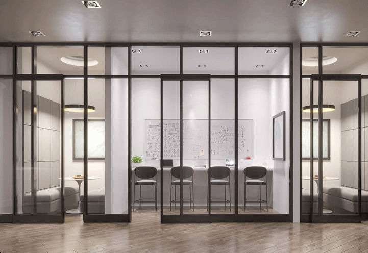A modern conference room with glass walls inside one of the new condos in GTA. There's a long table with six black chairs, a whiteboard covered in sketches, two windows, and a circular ceiling light. There are two small seating areas with round tables and gray chairs on either side.