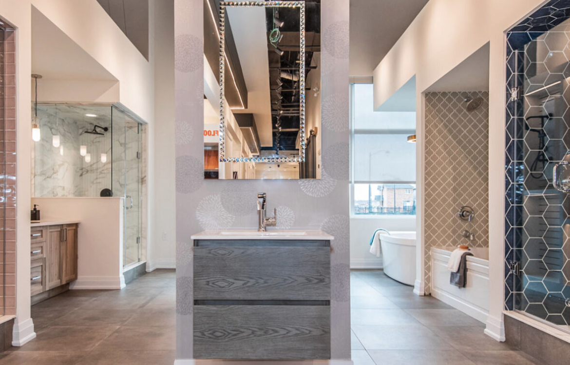 A stylish showroom display featuring modern bathroom designs, perfect for pre-construction homes. The centered vanity with a rectangular mirror is flanked by diverse shower and bathtub setups showcasing contemporary tiles, fixtures, and finishes. The overall look is sleek and sophisticated.