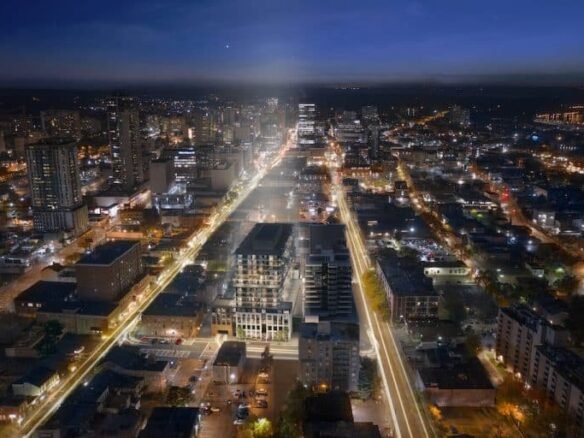 A nighttime aerial view of a city with brightly lit streets and buildings. The long exposure captures light trails of vehicles, highlighting busy roads, while the city extends outward with a mix of high-rise and low-rise structures illuminated against the dark sky. New homes in GTA are scattered among these lights.