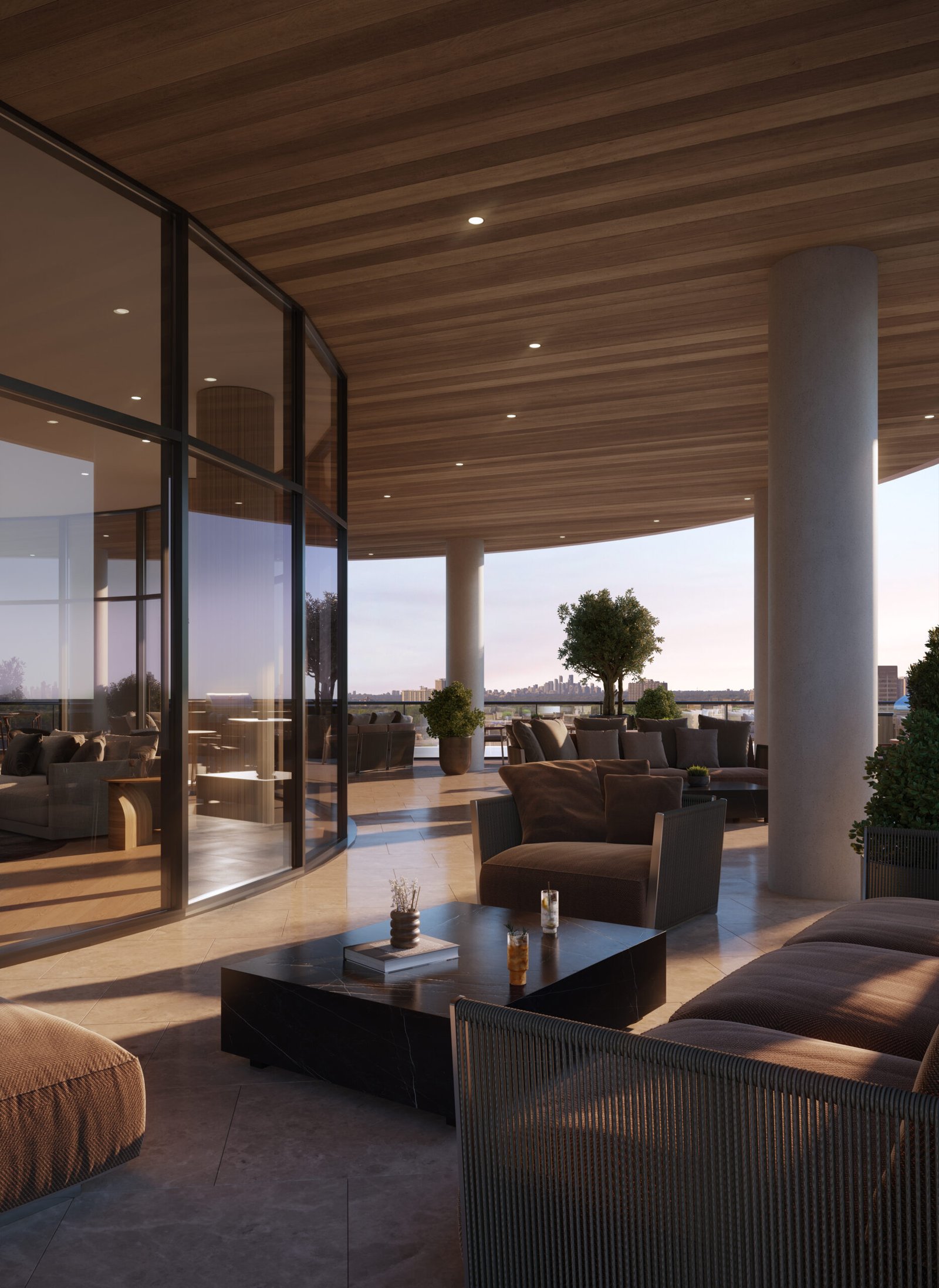 A modern, luxurious outdoor terrace with a wooden ceiling has comfortable seating, potted plants, and glass walls. The sun is setting, casting a warm glow over the scene. Two beverages from LSQ 2 sit on a low table, with distant cityscape views in the background.