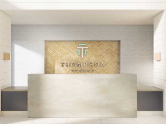A modern reception desk with a light gray counter stands in front of a wall featuring a wood herringbone pattern. Above the desk, the text "THOMPSON TOWERS" is displayed alongside a stylized "TT" logo. The area, well-lit with neutral tones and minimalist design, highlights the appeal of new condos in GTA.