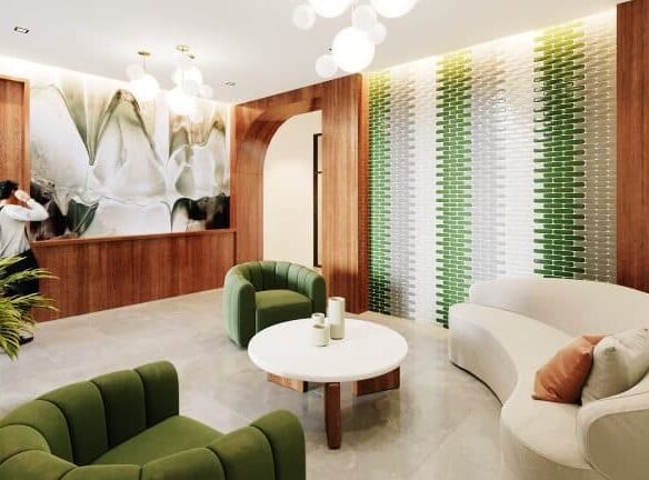 The lobby at Motto Condos features green armchairs, a white circular table, and a curved white sofa with an orange cushion. The walls are adorned with wood paneling, a green and white tiled design, and a large floral mural. Ceiling lights illuminate the space, and a plant is in the foreground.