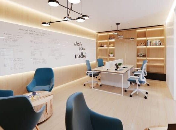A modern office space within Motto Condos features a whiteboard wall covered in notes and equations, a central table with chairs, and blue armchairs around a small wooden table. Shelves with books and plants are in the background, while the text "What's your model?" adorns the wall.