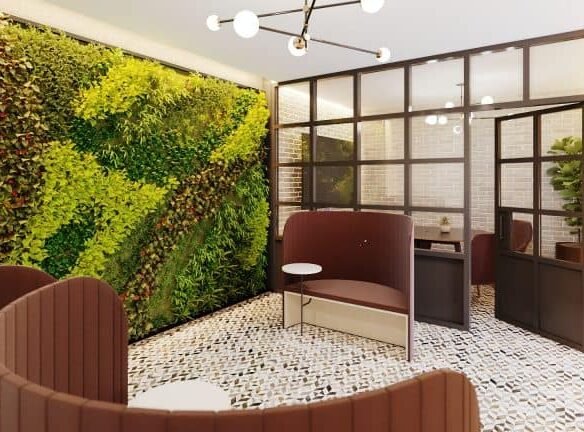 A modern lounge area at Motto Condos features curved, brown seating booths, a small table, and a large vertical garden on one wall. Glass partition walls with black frames divide the space, while the floor is patterned with small tiles in various shades of brown and white. Experience the best in urban living here.
