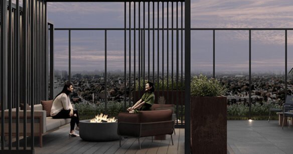 Two people sit around a fire pit on a rooftop terrace at dusk. They are surrounded by modern outdoor furniture, potted plants, and a view of new homes in the GTA sprawled out in the distance. The sky is cloudy with hues of pink and purple.