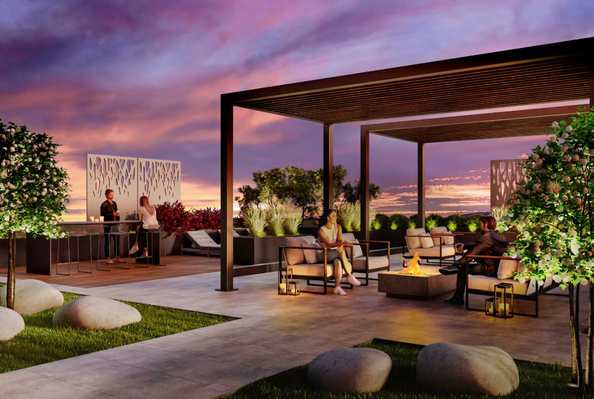 A stylish rooftop lounge at sunset features modern pergolas, comfortable seating, a fire pit, and lush greenery. People are socializing at a bar counter and sitting on armchairs, enjoying the elegantly landscaped space with ornamental rocks and illuminated panels—perfect for those considering new condos in GTA.
