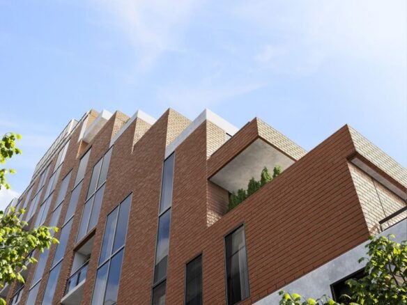 The Six99 Condos is a modern multi-story brick apartment building with large windows under a clear blue sky. The structure features sharp, angular designs with a corner balcony adorned with greenery. Trees partly frame the view, adding a natural element to the urban scene.