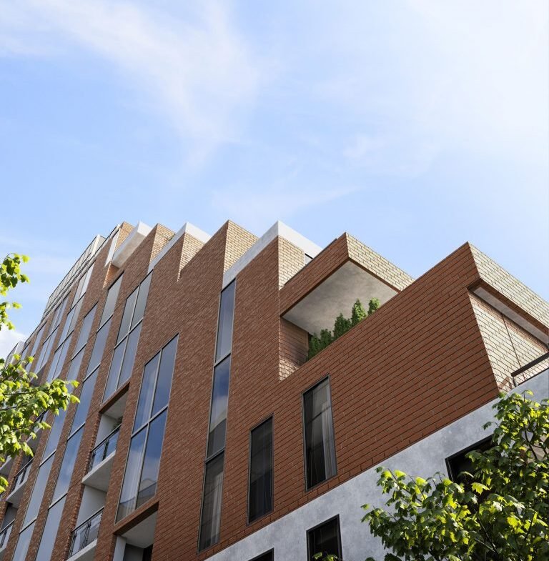 The Six99 Condos is a modern multi-story brick apartment building with large windows under a clear blue sky. The structure features sharp, angular designs with a corner balcony adorned with greenery. Trees partly frame the view, adding a natural element to the urban scene.