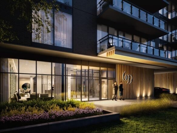 The image shows the modern entrance of Six99 Condos at dusk. The exterior features large glass windows and wooden paneling. Two people are walking towards the door, and landscaped greenery is in the foreground.