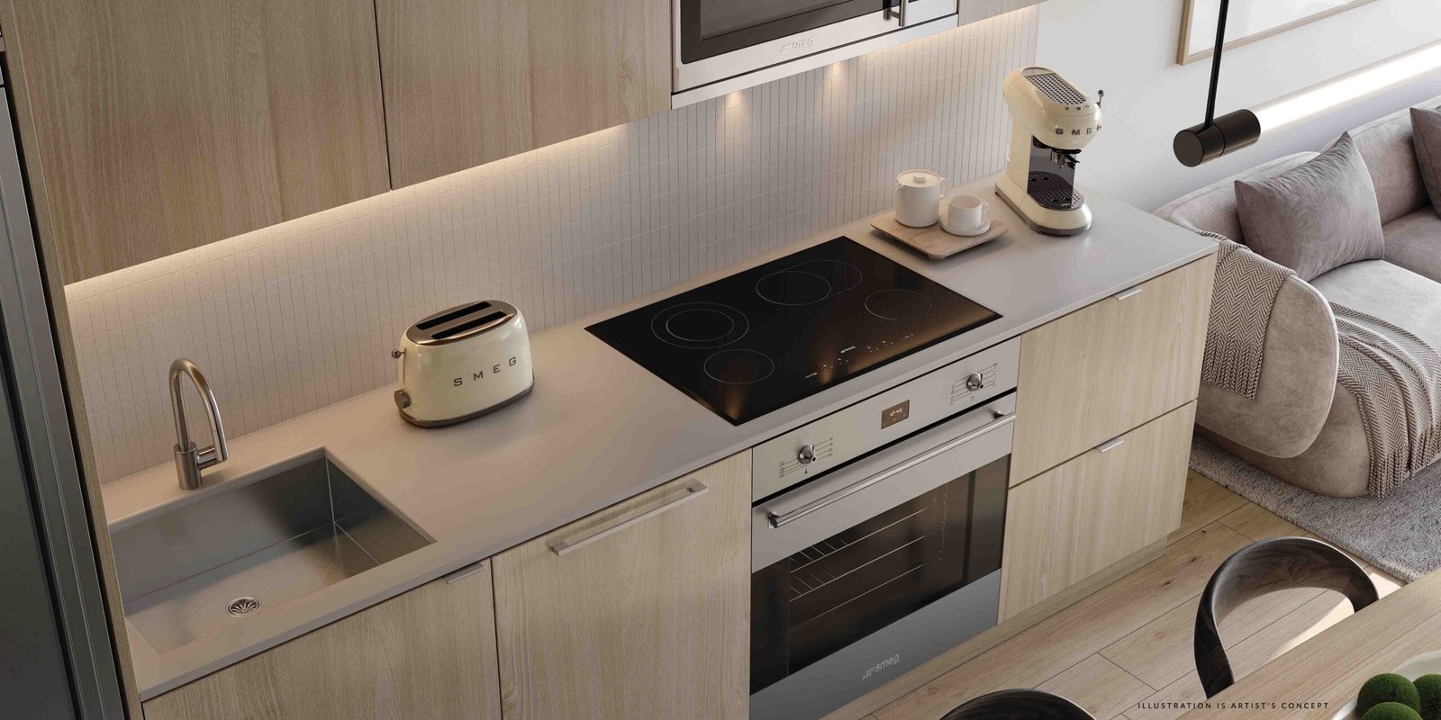 Modern kitchen interior featuring light wood cabinets, a sleek induction stove, built-in oven, and small appliances in a pre-construction home. A cozy seating area with a gray sofa is visible adjacent