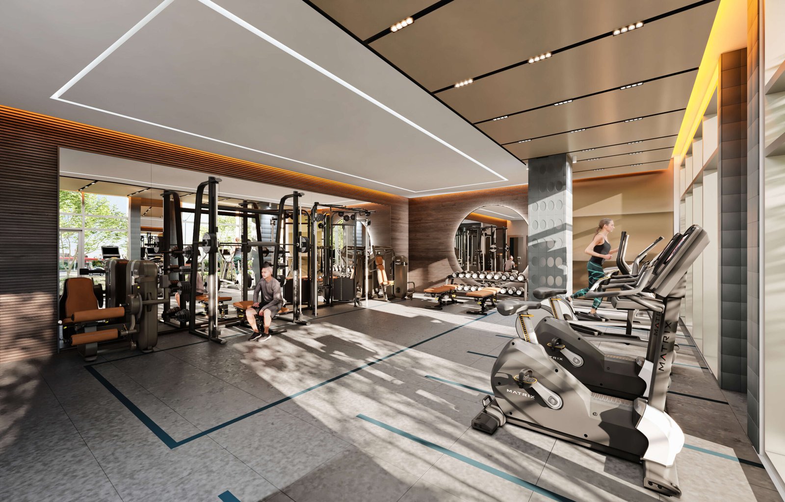 A modern gym with exercise machines, including treadmills, weightlifting equipment, and stationary bikes. A person uses the equipment as natural light streams in from large windows, creating a bright and inviting atmosphere—perfect for those living in new condos in Brampton nearby.