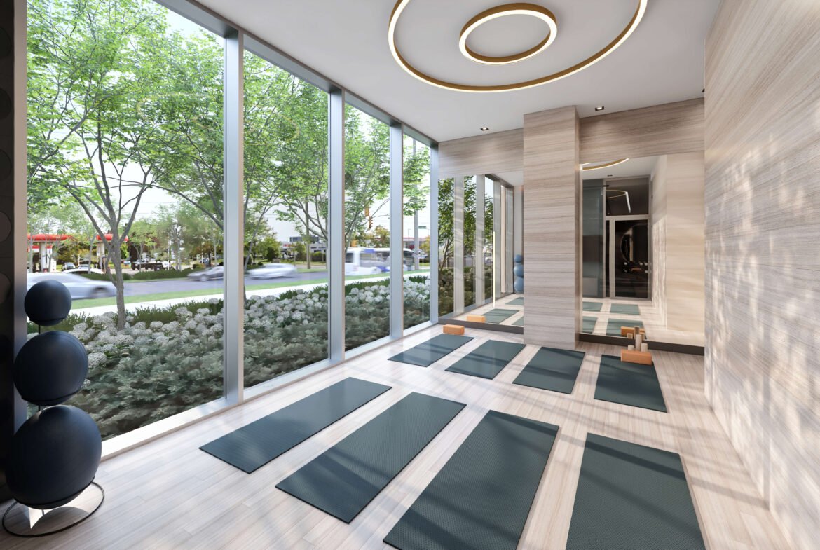 A modern, serene yoga studio with floor-to-ceiling windows showcases a landscaped outdoor view. Green yoga mats are neatly arranged on the wooden floor, while circular ceiling lights enhance the elegance of the minimalist design—mirroring the tranquility found in new homes in Toronto.