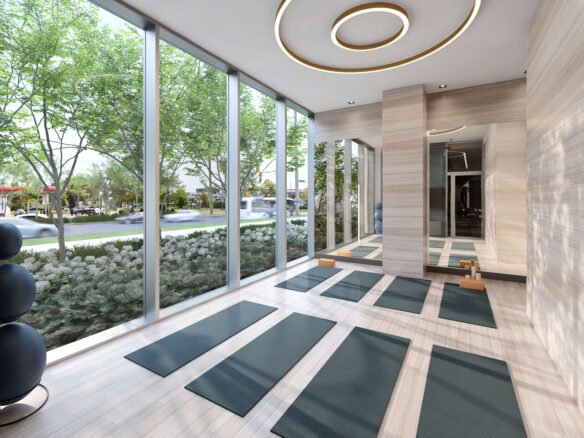 A modern, serene yoga studio with floor-to-ceiling windows showcases a landscaped outdoor view. Green yoga mats are neatly arranged on the wooden floor, while circular ceiling lights enhance the elegance of the minimalist design—mirroring the tranquility found in new homes in Toronto.