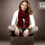 A person with long hair sits cross-legged on a transparent chair, wearing a white shirt, ripped jeans, and a red and black checkered scarf. They have a confident expression. The words "Beyond Condos" appear in the upper right corner of the image.