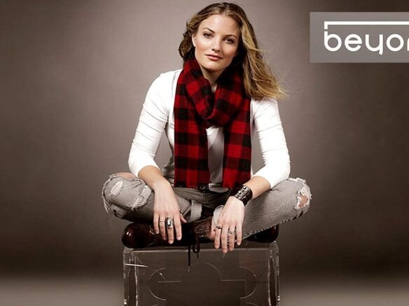 A person with long hair sits cross-legged on a transparent chair, wearing a white shirt, ripped jeans, and a red and black checkered scarf. They have a confident expression. The words "Beyond Condos" appear in the upper right corner of the image.