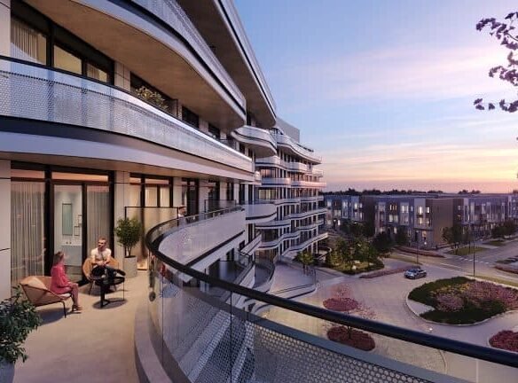 Two people enjoy a conversation on a balcony of a modern apartment building during sunset, overlooking a residential area with landscaped gardens, in view of New condos.
