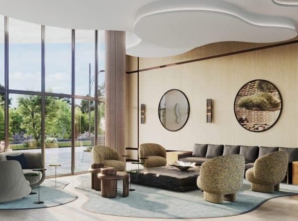 A modern living room in New Condos with large windows overlooking greenery, featuring a gray sectional sofa, blue armchairs, unique stone coffee tables, and stylish wood paneling with circular art pieces