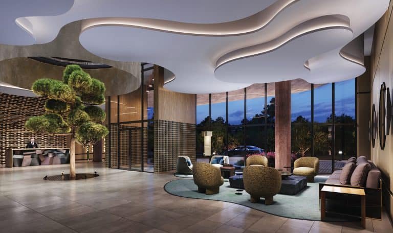 Modern hotel lobby at dusk featuring sculptural white ceiling, stylish furniture, and floor-to-ceiling windows showing outdoor views.