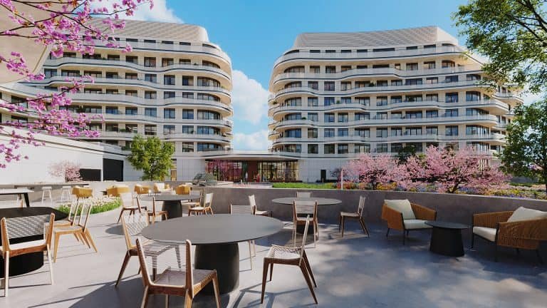 Modern outdoor café space with tables and chairs in a courtyard, framed by blossoming pink trees, showcasing New condos with curved, contemporary architecture in the background under a clear blue sky.