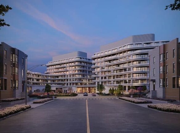 Modern residential complex at twilight with well-lit, multi-story buildings and a landscaped front area, viewed from a central driveway. Featuring New Condos and Pre Construction Homes.