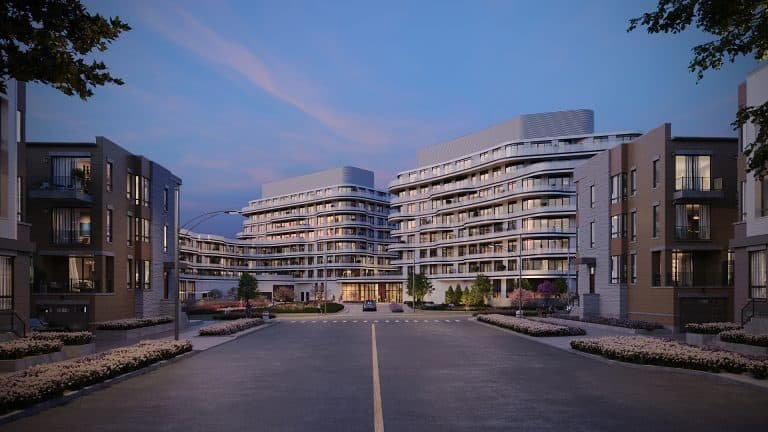 Modern residential complex at twilight with well-lit, multi-story buildings and a landscaped front area, viewed from a central driveway. Featuring New Condos and Pre Construction Homes.