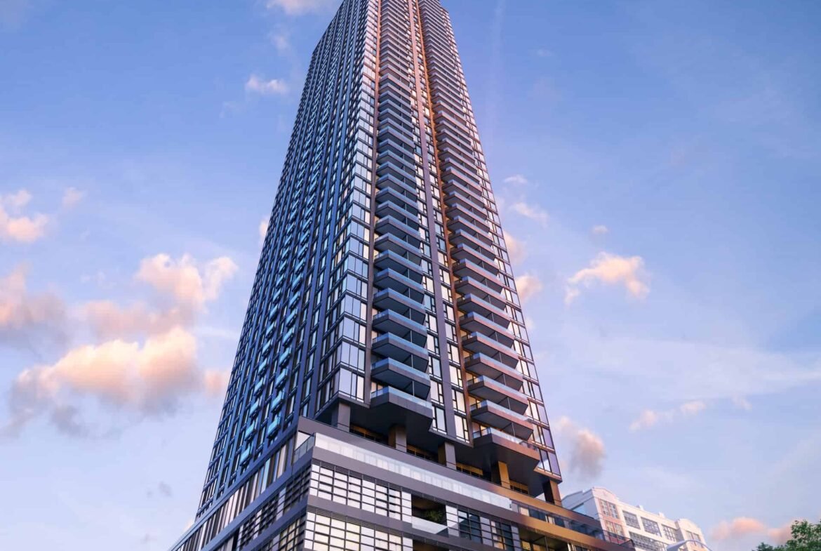 The sleek, glass exterior of the tall, modern skyscraper stands out against a blue sky with soft clouds. Its prominent angular design echoes the innovative architecture of new homes in Brampton. At its base, trees and a vehicle enhance the sense of scale.