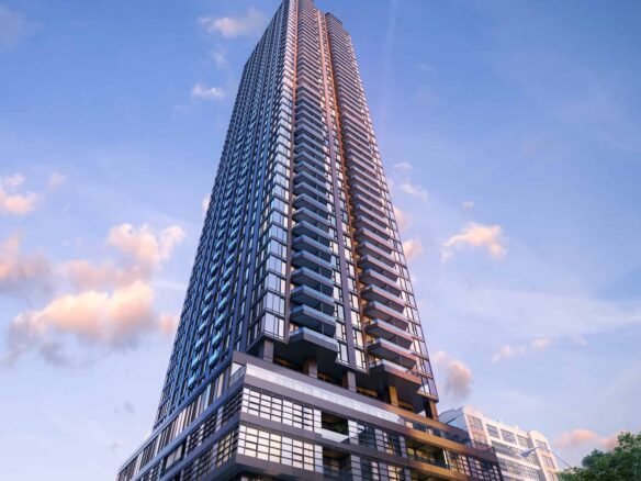 The sleek, glass exterior of the tall, modern skyscraper stands out against a blue sky with soft clouds. Its prominent angular design echoes the innovative architecture of new homes in Brampton. At its base, trees and a vehicle enhance the sense of scale.