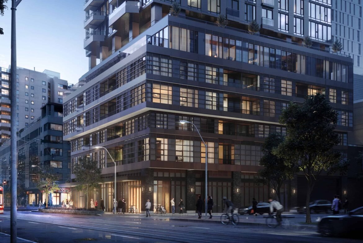 A street view captures a modern city corner at dusk, highlighting a multi-story building with glass windows aglow. Pedestrians stroll along the sidewalk as vehicles and a streetcar navigate the road. Trees line the area, complementing the urban landscape that boasts new condos in GTA.