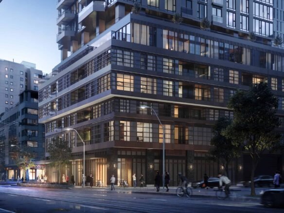 A street view captures a modern city corner at dusk, highlighting a multi-story building with glass windows aglow. Pedestrians stroll along the sidewalk as vehicles and a streetcar navigate the road. Trees line the area, complementing the urban landscape that boasts new condos in GTA.