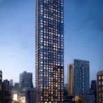 A towering skyscraper with illuminated windows stands against a twilight sky, surrounded by other buildings in a bustling urban area. Streetlights and car trails light up the busy road below, as nearby new condos in the GTA promise luxurious living above the vibrant city scene.
