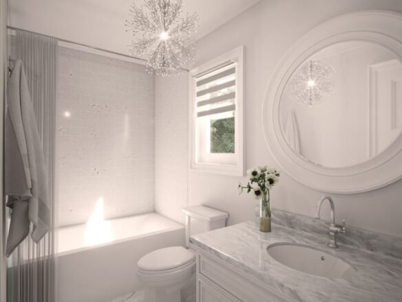 A bright, modern bathroom in one of the new homes features a marble countertop sink, a round mirror, a toilet, and a bathtub. A chandelier-style light fixture hangs above, and the window has a striped blind. A small vase with flowers graces the counter.