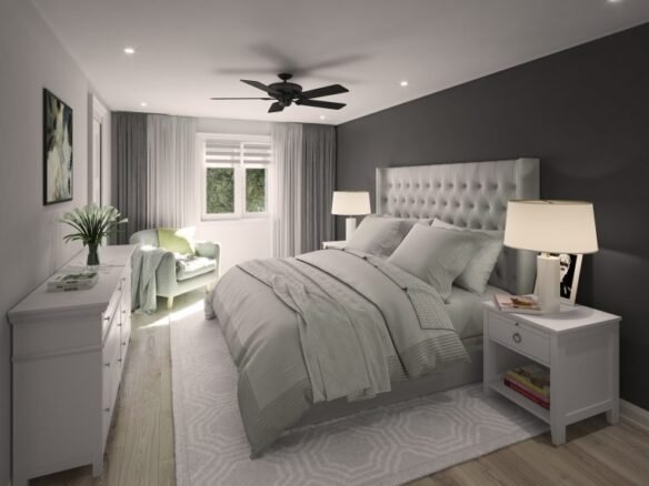 A modern bedroom in one of the new homes in GTA features a large bed with a grey padded headboard and light grey bedding. Twin nightstands flaunt lamps, while a green armchair sits by the window under a ceiling fan. The room's dark and light grey walls are complemented by a dresser and potted plant.