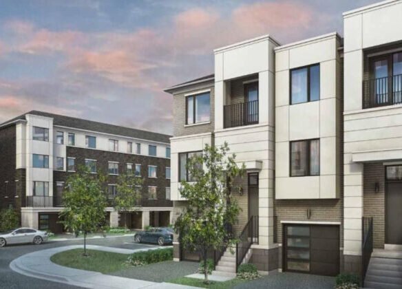 A modern apartment complex with multiple three-story buildings showcases white and dark brick exteriors. The scene includes trees, a circular driveway, and parked cars under a cloudy sky at sunset. Discover the charm of pre-construction homes in this serene setting.