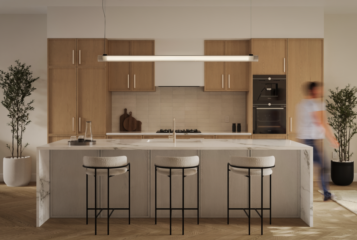 A modern kitchen in a new condo with a marble island and three cushioned barstools. Light wood cabinets complement the linear pendant light above. Stainless steel appliances and minimal decor, including plants, complete the space while a person appears slightly blurred in motion.