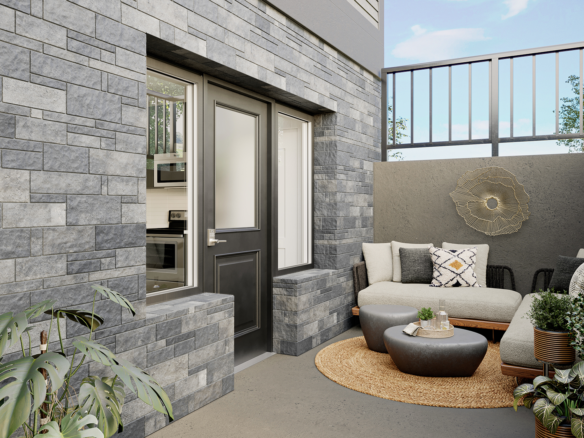 A cozy outdoor patio with a gray brick wall, a beige sectional couch adorned with patterned pillows, and a modern touch from the round woven rug and small table. The area, featuring potted plants and a tall railing, offers a tranquil and stylish Marquis setting.