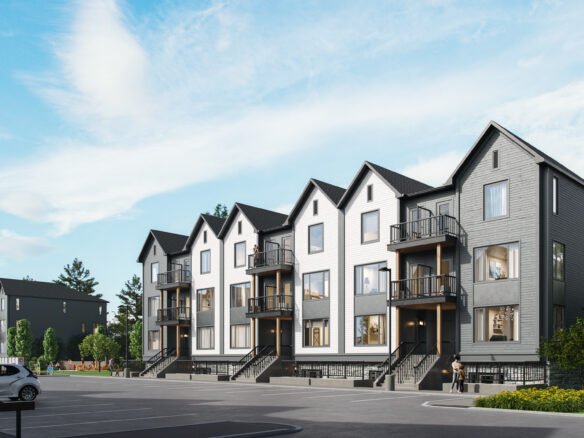 A modern residential complex showcases new homes arranged in two rows of identical, multi-story townhouses. The buildings feature gray and white exteriors with gabled roofs and small balconies. A spacious parking lot sits in the foreground, surrounded by streetlights and a few trees.
