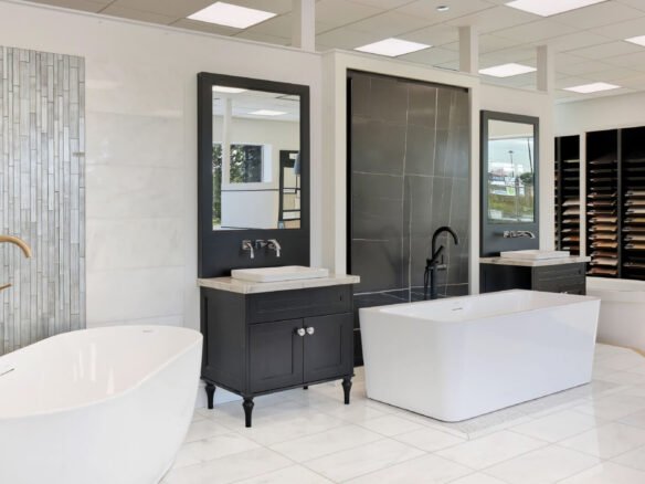 A modern bathroom showroom by Royal Pine Homes in Mayfield Village features an elegant design with freestanding and rectangular tubs, black vanities paired with mirrors, chrome faucets, and a wall display of tile samples.