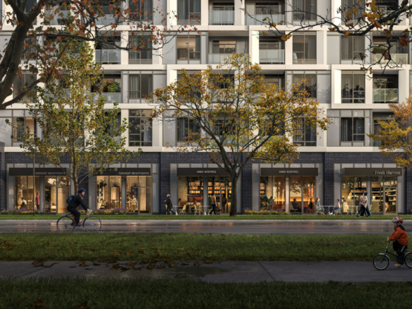 Discover new condos in the GTA within this modern apartment building, boasting retail shops on the ground floor. People stroll and ride bicycles along a tree-lined sidewalk, with autumn leaves scattered across the grass.