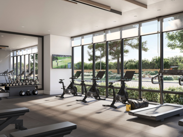 A modern gym with large windows offers a leafy view and includes exercise bikes, treadmills, and weightlifting equipment. Perfect for residents of new homes in Toronto, a TV displays sports while natural light fills the room, highlighting a clean and organized space.