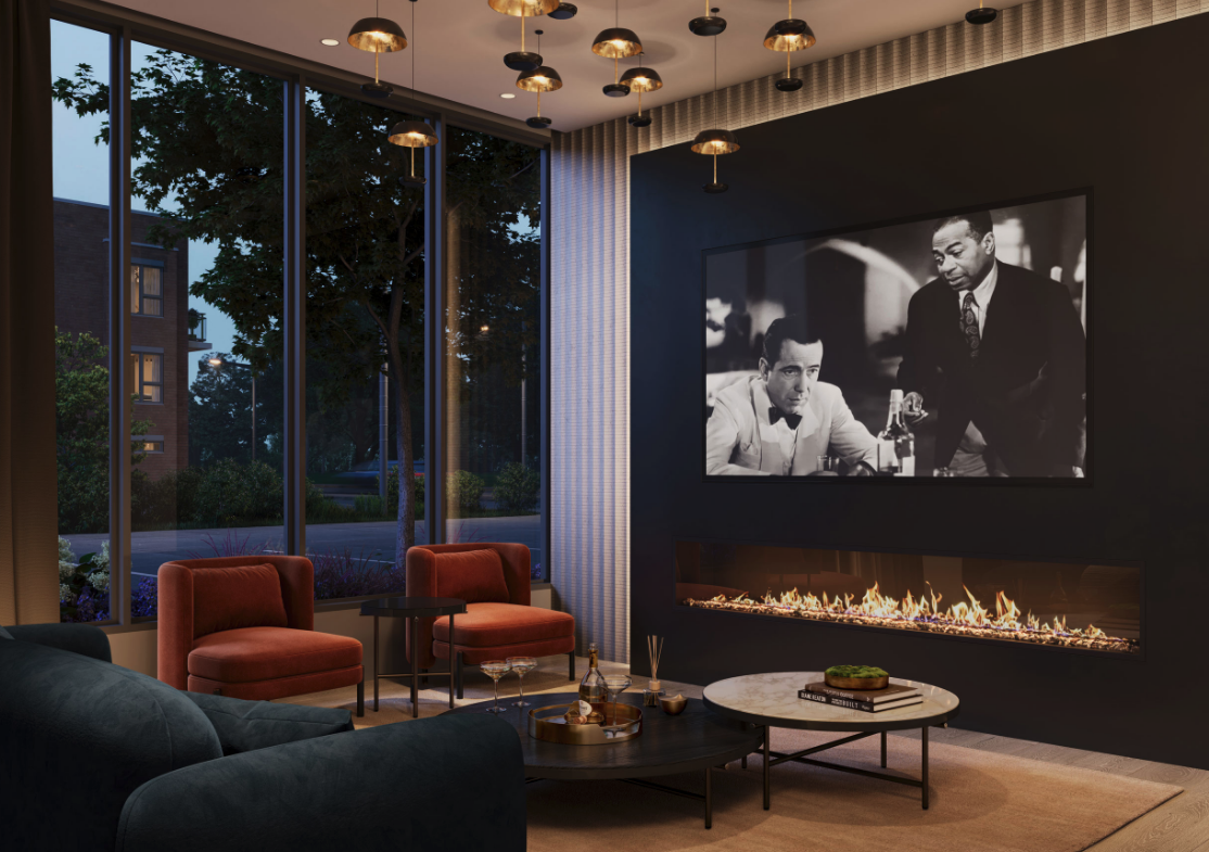 A modern living room in new homes features a sleek fireplace, a large black-and-white movie still on the wall, two orange armchairs, a dark sofa, and a round coffee table. Floor-to-ceiling windows reveal an evening cityscape, while hanging lights add warmth.